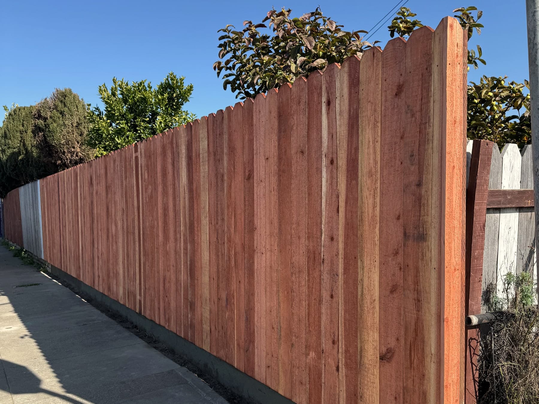 Redwood fence project with clean vertical boards along a sidewalk.